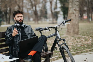 A handsome businessman conducts remote work in a serene park setting, using a laptop with his bicycle nearby.