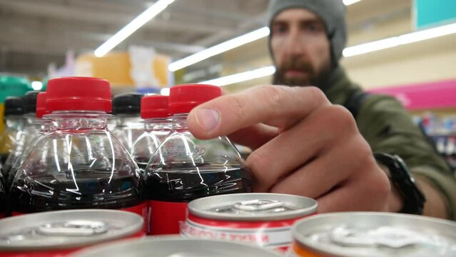 Close-up of many plastic cola bottles in a drinks department and a buyer with a shopping basket takes two
