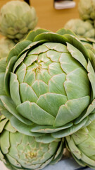 Fototapeta premium Close-up of a fresh green artichoke on display at a farmers market, ideal for vegetarian cuisine and healthy eating content, related to World Vegetarian Day