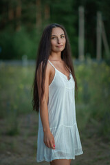 Fototapeta premium Portrait of a young beautiful dark-haired girl in a light dress in a summer field.