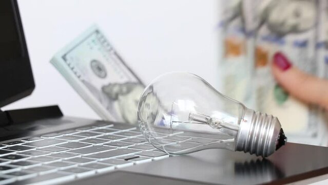 A girl counts dollars against the background of an incandescent light bulb and a laptop, light tariff
