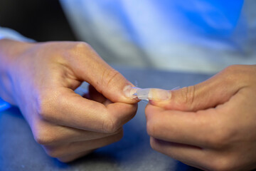 mains d'une femme réalisant sa manucure avec des capsules à coller sur ses ongles 