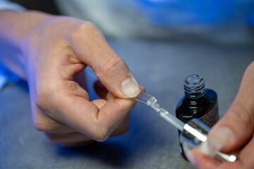 mains d'une femme réalisant sa manucure avec des capsules à coller sur ses ongles 