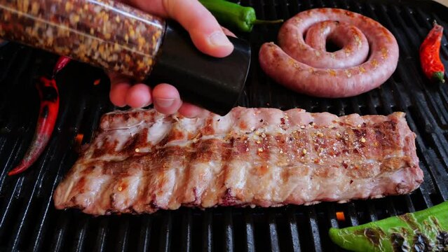 Chef Sprinkles Salt And Spices on pork ribs On Grill Rack. Cooking natural sausage on grill. Slow motion. Close up