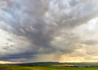 Rain falling from towering clouds on a rural landscape