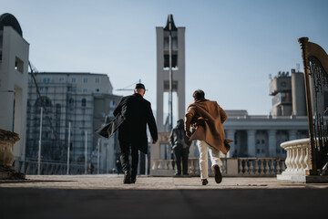 Back view of professional men in coats walking energetically in an urban setting, capturing a sense...