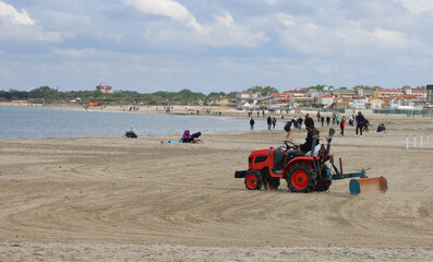 Red tractor for cleaning the sand on the beach by the sea before the arrival of the tourists