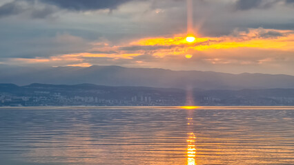 The sun setting behind mountains in Croatia. The Mediterranean Sea is calm and clear, reflecting...
