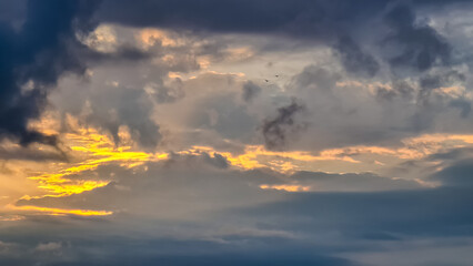 The setting sun hiding behind thick clouds. The clouds are colored yellow and orange. Many...