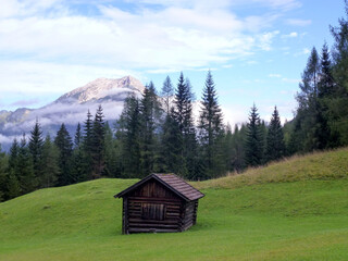 Picturesque landscape of the mountain slope in bright colors. In the foreground is an old wooden barn on the grass.