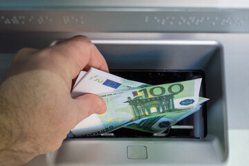a man's hand puts euro bills in the ATM tray to be credited to the account. mortgage repayment...
