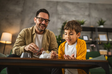 Father show son how to save money at piggy bank at home © Miljan Živković