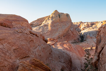 Obraz premium Panoramic sunrise view of arid landscape with striated red and white rock formations along the White Domes Hiking Trail in Valley of Fire State Park in Mojave desert, Overton, Nevada, USA. Road trip
