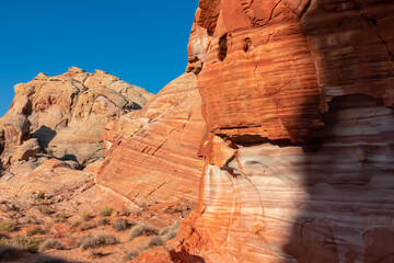 Scenic view on wall of striated red and white rock formations along the White Domes Hiking Trail in Valley of Fire State Park in Mojave desert, Nevada, USA. First sunlight touches arid landscape