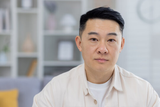 A clear, high-quality photo of a middle-aged Asian man looking directly at the camera with a calm expression, set against a softly blurred home background.
