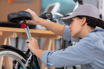 female bicycle mechanic repairing a bike in the workshop - obrazy, fototapety, plakaty