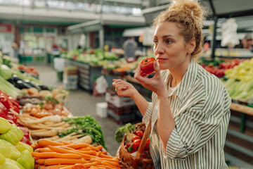 Portrait of shopper woman with basket smelling fresh tomato at market.