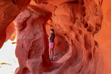 Woman standing in the fire cave and Windstone Arch in Valley of Fire State Park, Nevada, USA. Long, narrow slot canyon with sheer rock walls. Tranquil desert landscape of eroded sandstone formation © Chris
