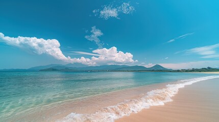 Pristine beach waters gently lapping the sand with distant mountains and a clear blue sky overhead