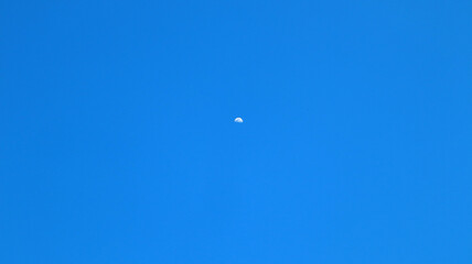Bright blue spring sky in the mountains and a small white daytime moon in the middle, a perfect...