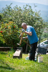 An elderly man is fixing his gardening tool. He is using suitable tools to fix his broken gardening tool. 
He is using his gardening tools for spring work in the orchard and wineyard.