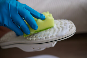 Applying cleaning foam from the bottle to white leather women's sneakers. Care for leather shoes, surface whitening.