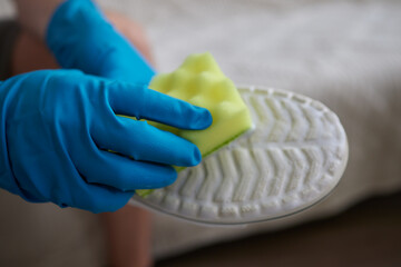Applying cleaning foam from the bottle to white leather women's sneakers. Care for leather shoes,...