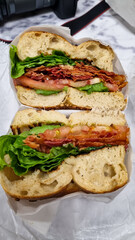 Typical New Yorker bagel with green salad, roasted beacon, and other ingredients on sesame bagel, prepared in a take-away foil. Nutritious breakfast.