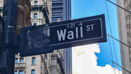 A close up on the sign, which points to the  Wall Street in New York City. There are tall buildings in the back. Famous landmarks. The sign has also a miniature of building along that street. - obrazy, fototapety, plakaty