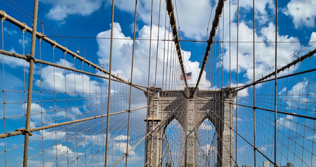 The gate of Brooklyn Bridge with a waving American flag on top of it contrasted with a blue sky...