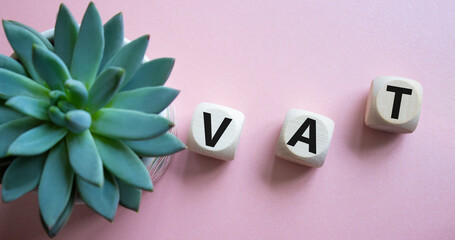 VAT - Value Added Tax symbol. Wooden cubes with word VAT. Beautiful pink background with succulent...
