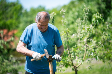 An elderly man is fixing his gardening tool. He is using suitable tools to fix his broken gardening...