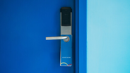 Close-up of a hotel room door featuring a stainless steel handle, electronic lock, and a blue Do...