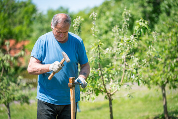 An elderly man is fixing his gardening tool. He is using suitable tools to fix his broken gardening...