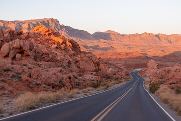 Panoramic sunrise view of endless winding empty road in Valley of Fire State Park leading to red Aztec Sandstone Rock formations and desert vegetation in Mojave desert, Overton, Nevada, USA. Freedom