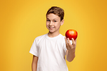 Positive little boy offering fresh red apple on camera