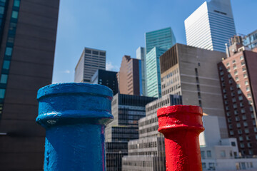 Two chimneys painted blue and red on the rooftop with the city skyline view and modern skyscrapers...