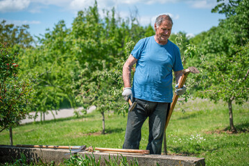 An elderly man is fixing his gardening tool. He is using suitable tools to fix his broken gardening...