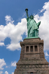 Fototapeta premium A close up on an iconic representation of freedom and independence, the Statue of Liberty with flaming torch on Liberty Island. The Lady on a Pedestal is surrounded by clouds. American history.