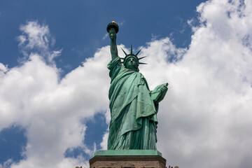 Fototapeta premium A close up on an iconic representation of freedom and independence, the Statue of Liberty with flaming torch on Liberty Island. The Lady on a Pedestal is surrounded by clouds. American history.