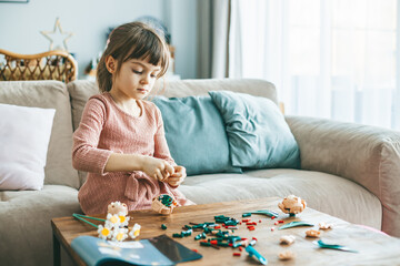 A charming little girl using small colorful construction pieces on a wooden table to craft flowers