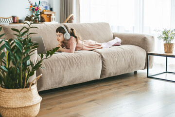 A little girl, lying on a sofa, captivated by the laptop screen in front of her, lost in her digital adventure. Concept: technology-infused relaxation, online education, technological entertainment