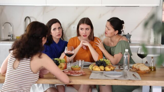 At cozy home gathering, attentive female friends comforting and supporting upset woman, discussing problems and giving advice over glass of wine