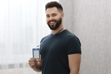 Happy young man with blank badge indoors