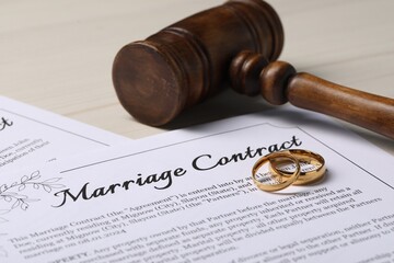 Marriage contracts, gold rings and gavel on light wooden table, closeup