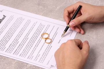 Man signing marriage contract at light grey table, closeup