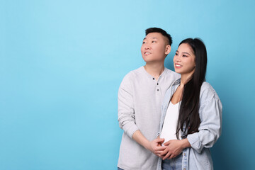 Pregnant woman and her husband on light blue background, space for text