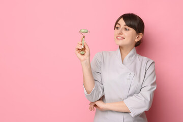 Cosmetologist with facial roller on pink background, space for text