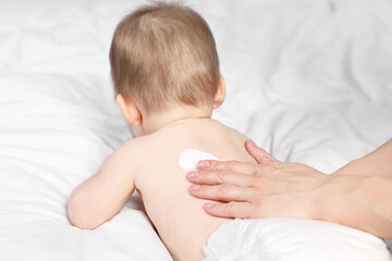 Woman applying body cream onto baby`s back on bed, closeup
