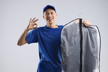 Dry-cleaning delivery. Happy courier holding garment cover with clothes and showing OK gesture on...